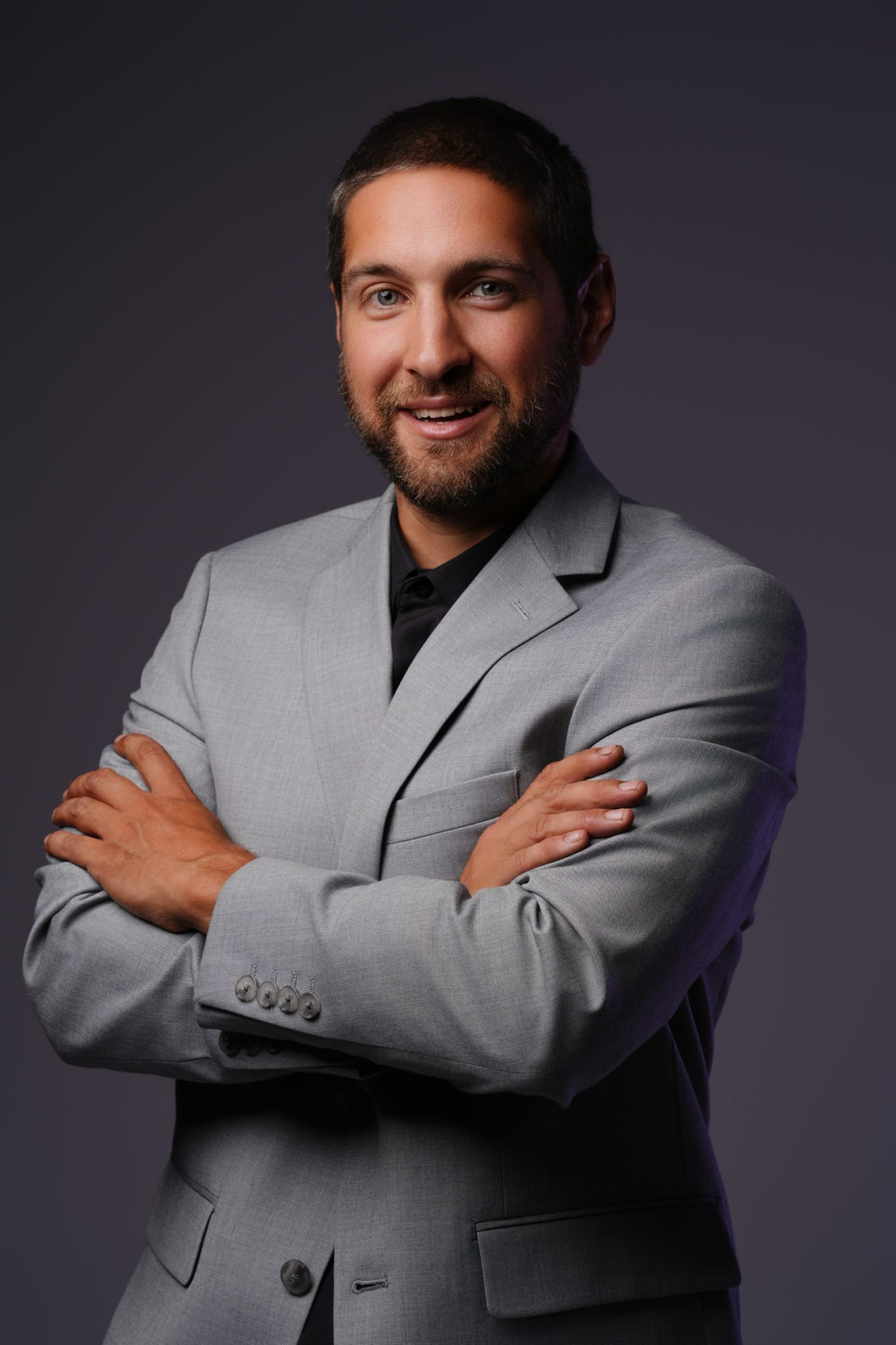 Justin Samuel Parsons portrait, arms crossed in a grey suit